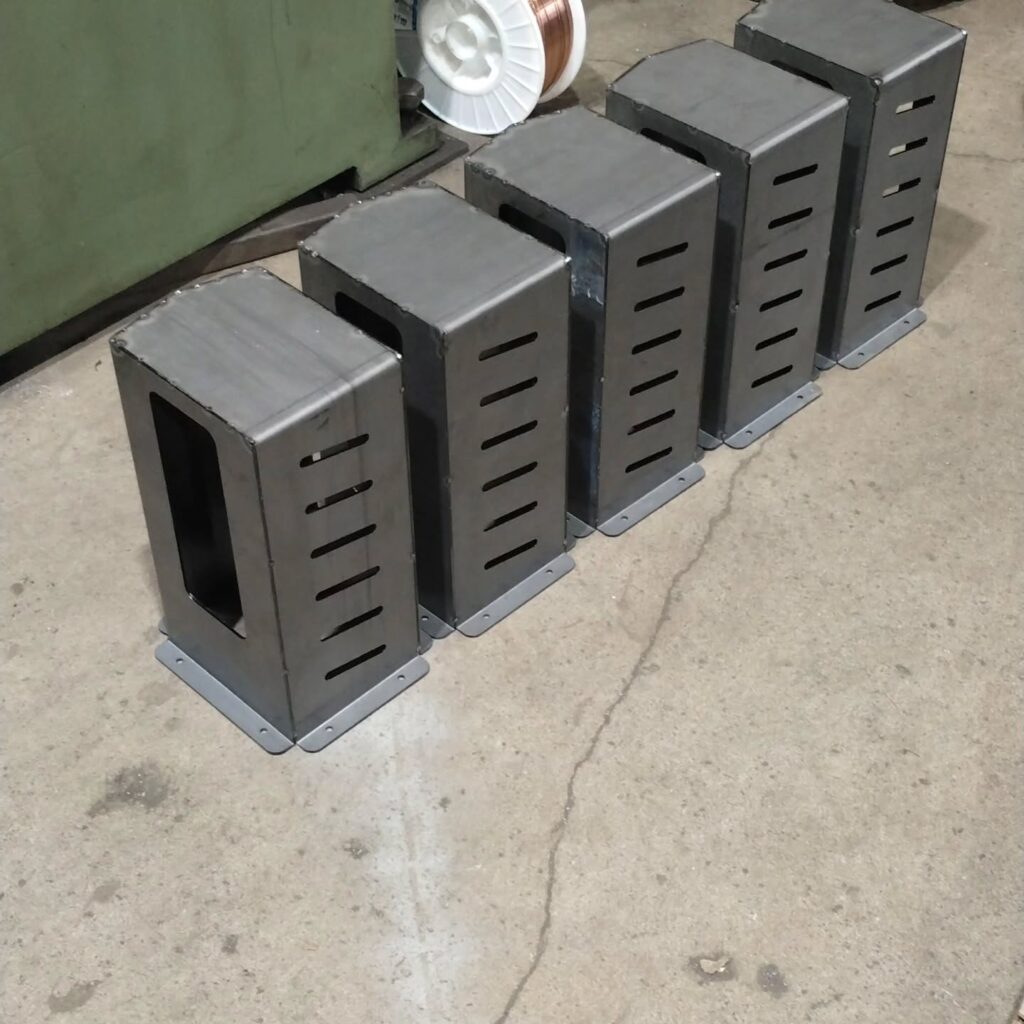 Five metal boxes with vertical slits, aligned on a concrete floor. These appear to be storage units, possibly used in an industrial setting.