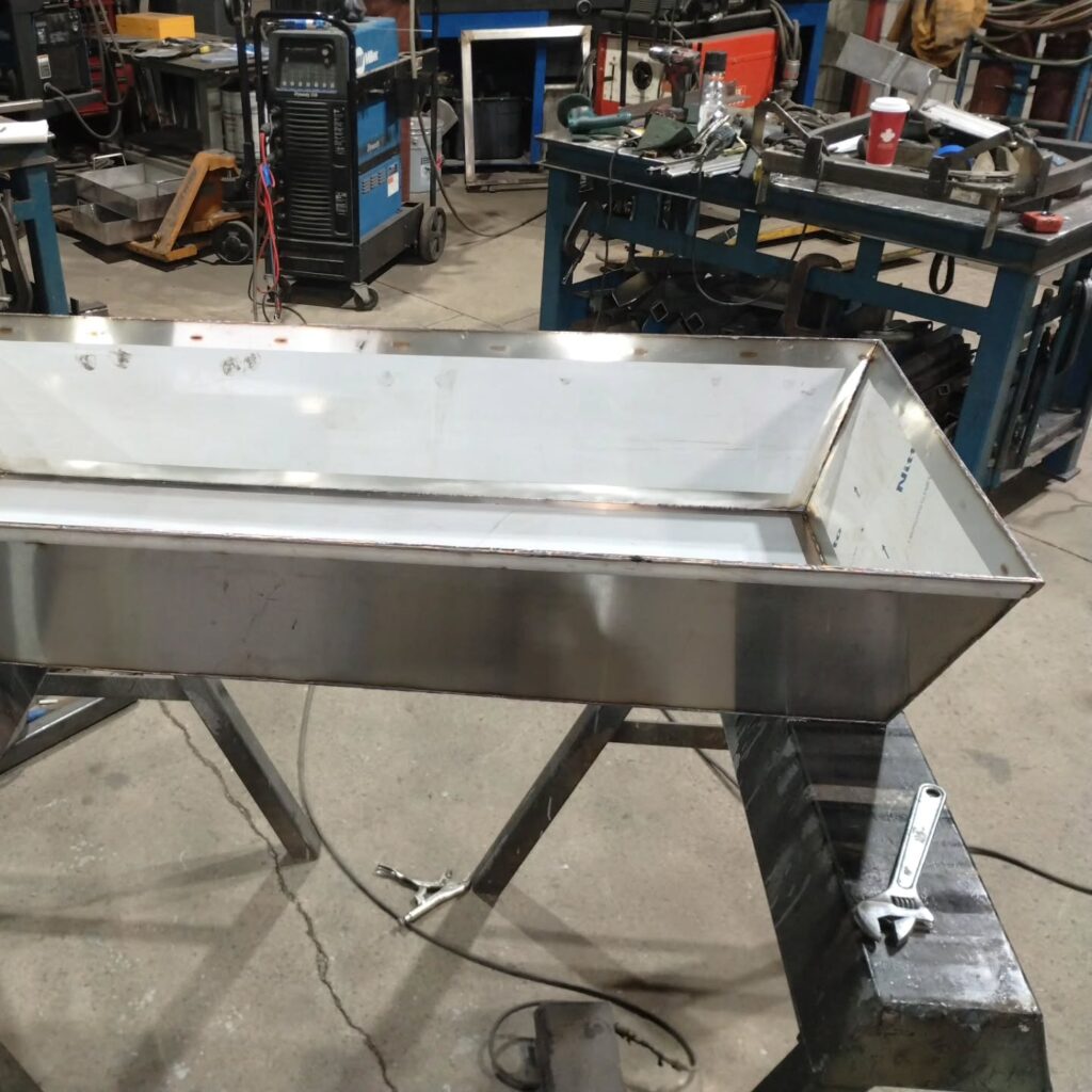 Stainless steel fabrication with a large rectangular container on a workbench, showcasing precision welding in a workshop environment.