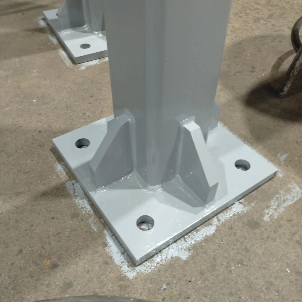 Gray steel column base with mounting holes, anchored to a concrete floor, showcasing industrial support structure preparation.