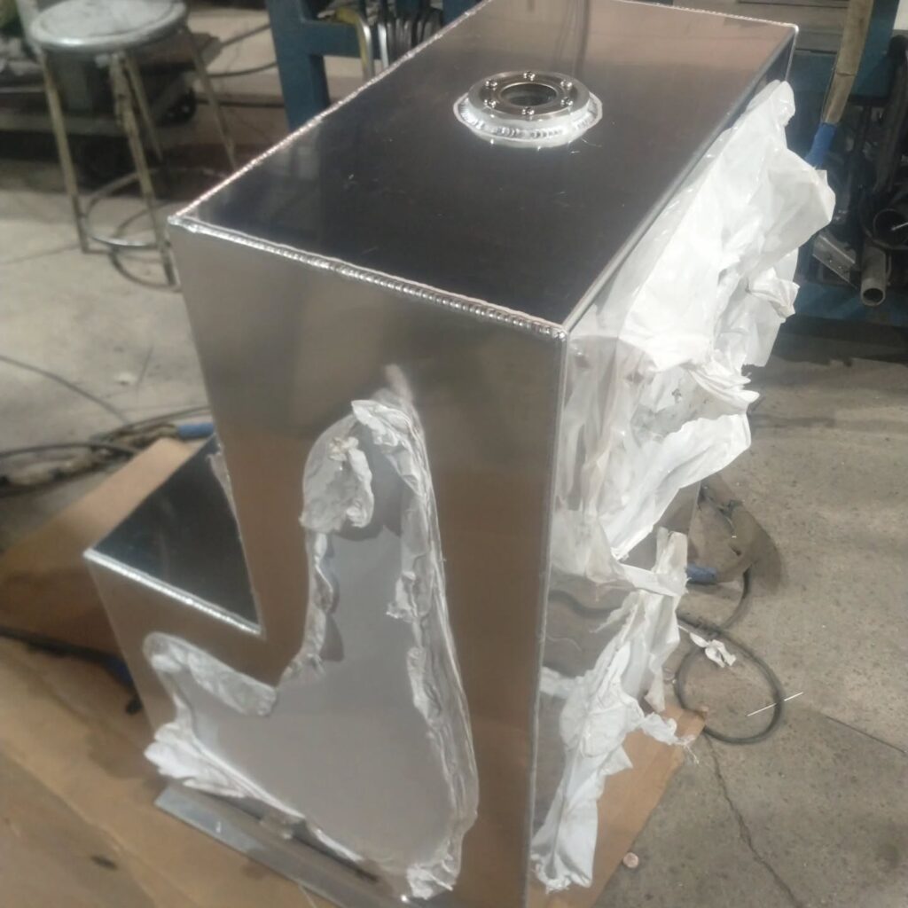 Polished metal structure with a protective wrapping, showcasing an intricate design. Set in a workshop environment, it highlights craftsmanship in metalworking.