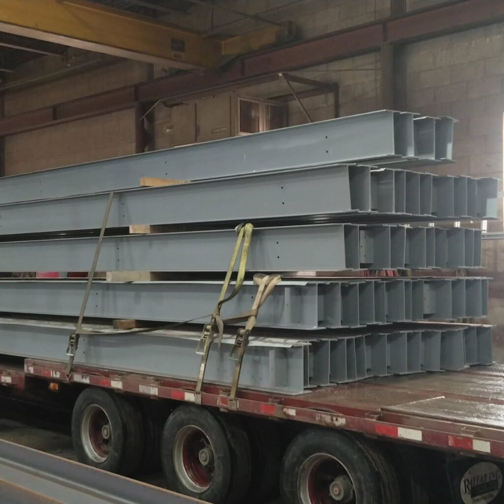 Steel beams stacked on a flatbed truck inside a warehouse, prepared for transportation. Essential for construction projects.