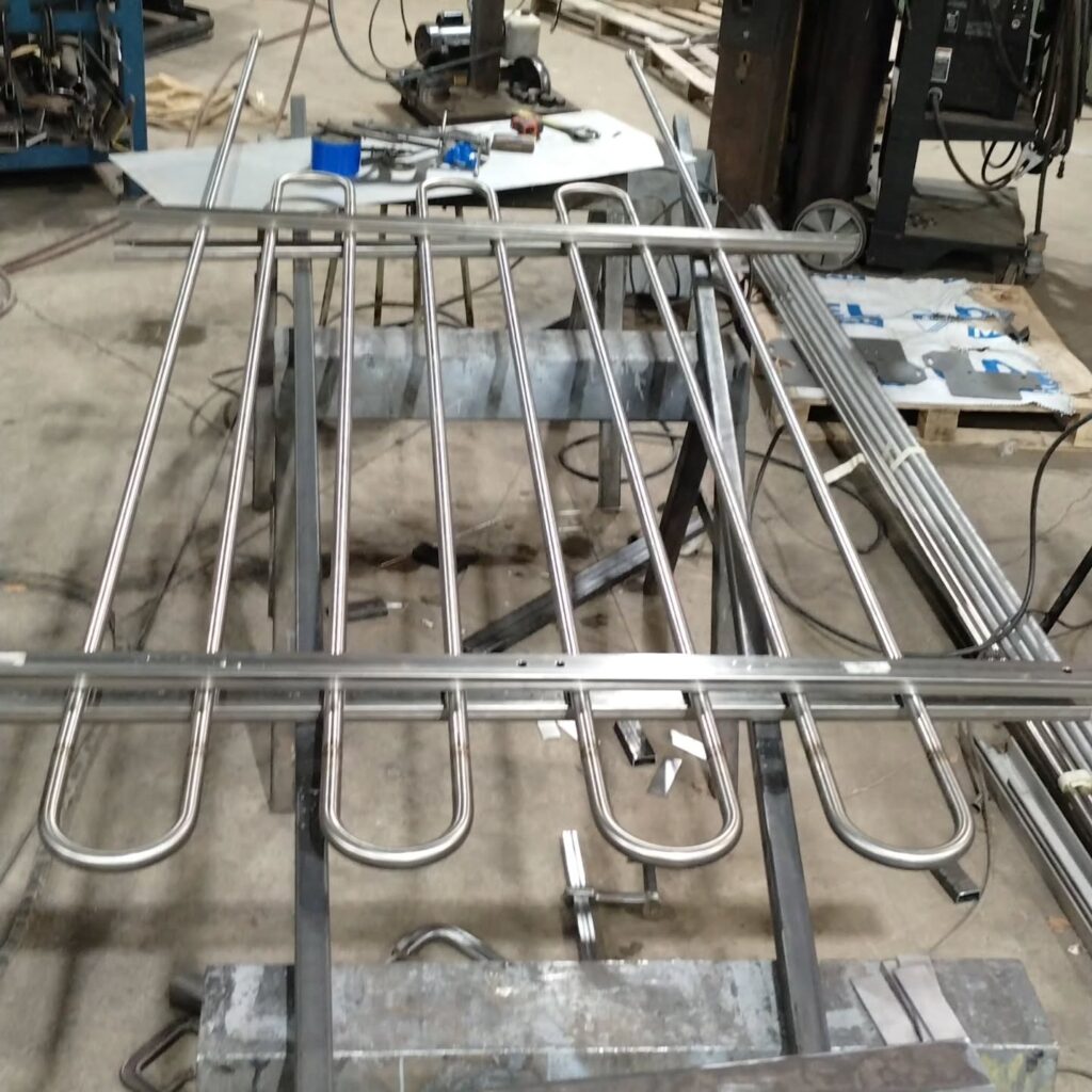 Stainless steel rods arranged in a grid on a workshop bench, showcasing fabrication processes for industrial components.