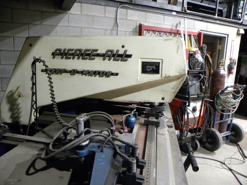 Industrial metalworking machine labeled "Pierce-All" in a workshop, showcasing tools and equipment essential for fabrication tasks.
