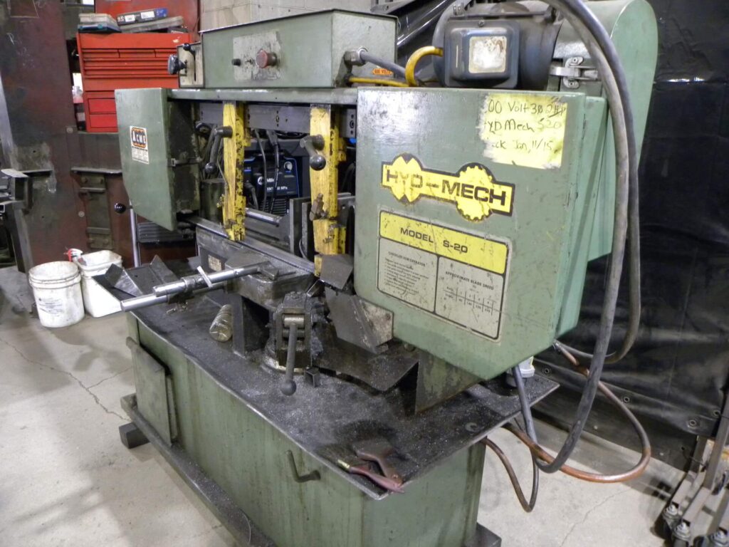 Hyd-Mech S-20 band saw machine in a workshop setting, showcasing its operational components and maintenance details. Essential for metal cutting tasks.